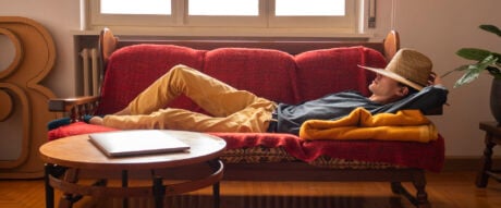 Young man wearing a hat on the sofa, earning money as he rests through passive income.