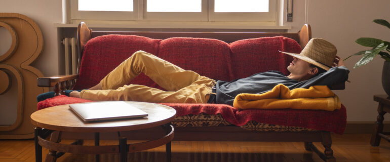 Young man wearing a hat on the sofa, earning money as he rests through passive income.