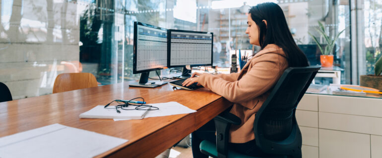 Investment banker sits at desk looking at monitors with data on them.