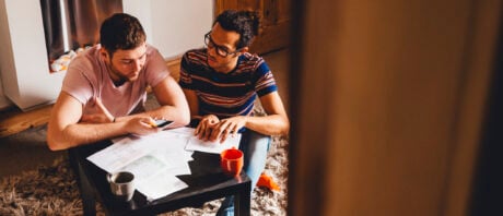 Male couple sits at living room coffee table discussing bonds in Canada.