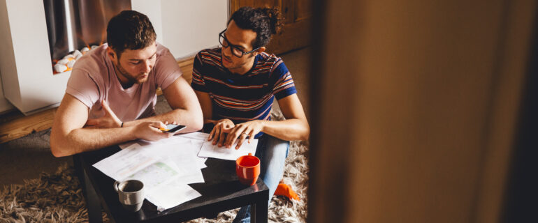 Male couple sits at living room coffee table discussing bonds in Canada.