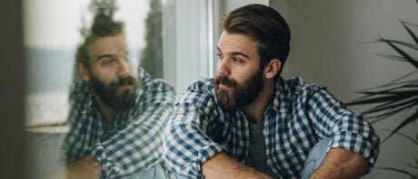 Young pensive man looks out window while pondering recession in Canada.