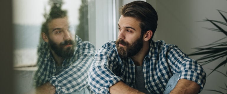 Young pensive man looks out window while pondering recession in Canada.