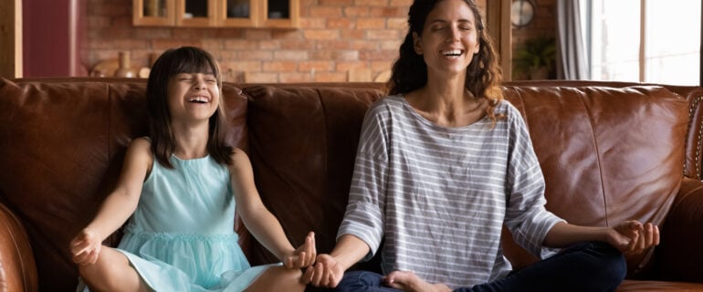 Happy young Hispanic mother and girl meditating on the couch, smiling with closed eyes after checking the personal loan rate to pay for the home reno.