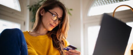 A young woman wearing yellow sweater shopping online on her laptop and paying with her low-interest credit card