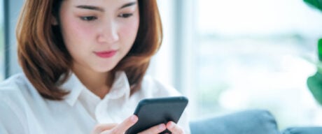 Asian woman holding a smartphone, Waiting to load her BMO Performance Chequing Account details.