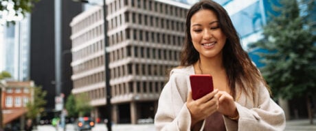 Asian woman using phone on the street to send money.