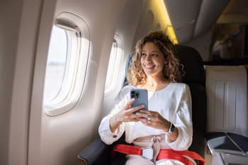 Latin American female traveler using her cell phone in an airplane and looking through the window
