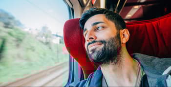 Happy young man is traveling first class on a train sitting and smiling looking out through the window