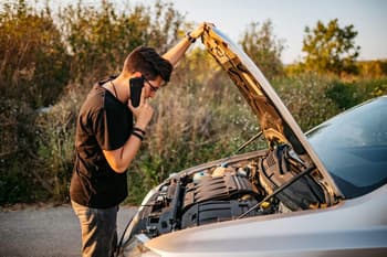 Adult looking at open hood of car and calling roadside assistance