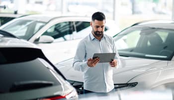 Man at car dealership researching cars on tablet