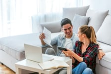 A cheerful young couple in their home using a laptop to analyze their finances for taking out an RRSP loan.