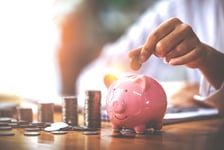 A person putting a coin in a piggy bank, which is sitting on a table.