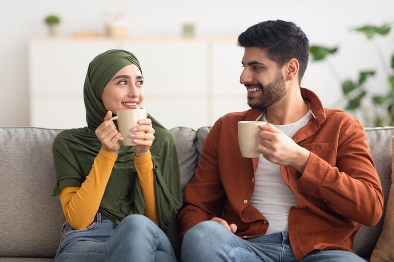 Happy Middle Eastern couple having coffee holding cups at home.