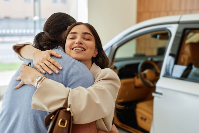 A smiling woman embracing her partner after a successful car purchase at a dealership center.