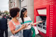Two girls smile as they take the money from the ATM for shopping.