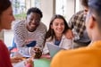 Cheerful multiracial group of young students working together with their classmates on a project sitting at a table in the faculty.