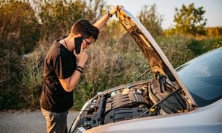 Adult looking at open hood of car and calling roadside assistance