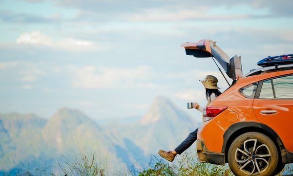 Woman sitting on car tailgate and looking at mountains