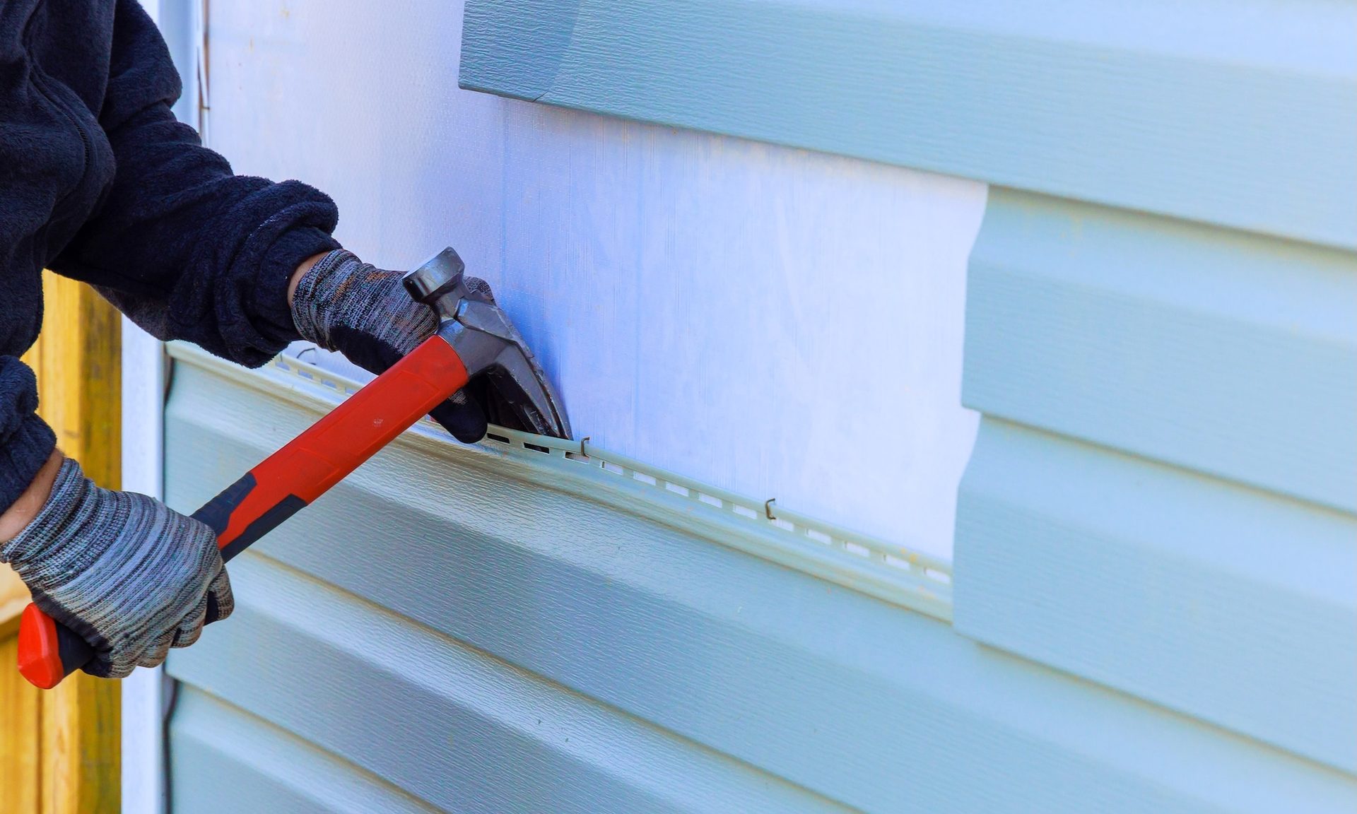Worker replacing vinyl siding on house