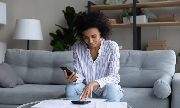 Person on couch with calculator and paperwork.
