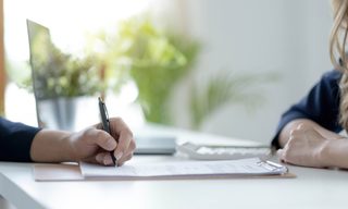 Close up of male hand signing document on clipboard at a work desk