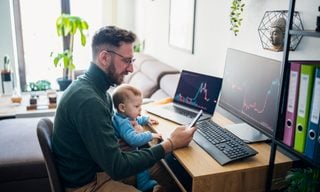 Person with baby looking at financial performance on computer in home office.