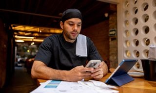 Latin American chef doing the books at a restaurant after closing and using an app on his cell phone