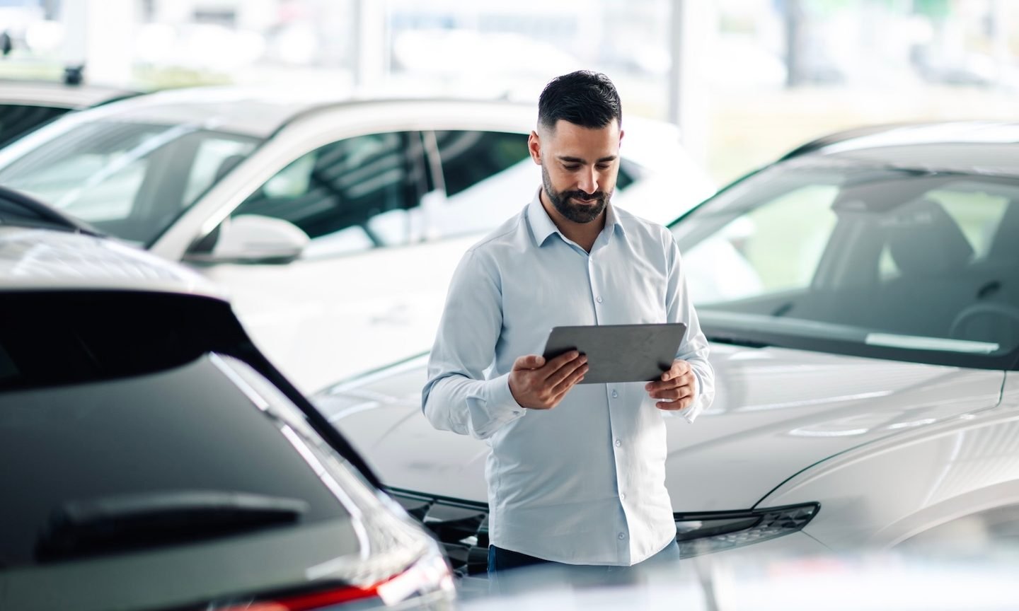 Man at car dealership researching cars on tablet
