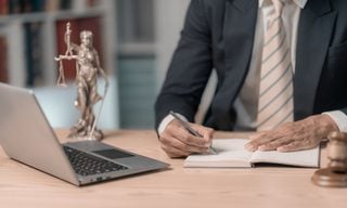 Lawyer writing in a notebook next to laptop