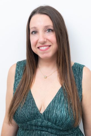 Woman business owner with long hair wears green dress and smiles at camera