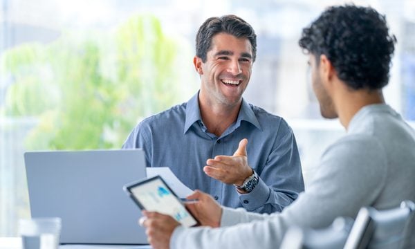 Two white men discuss finances in front of laptop and tablet